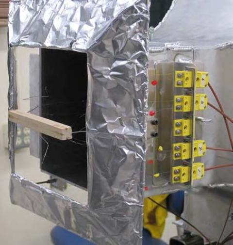 Thermocouple instrumented fuel particle in holder, thermocouple connectors, and reflecting shroud attached to wind tunnel